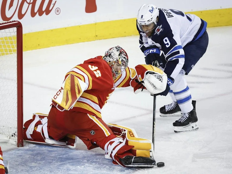 Winnipeg Jets’ Alex Iafallo, right, has the puck kicked away by a stickless Calgary Flames goalie Dustin Wolf during second period NHL hockey action in Calgary, Alta., Monday, Oct. 20, 2025.