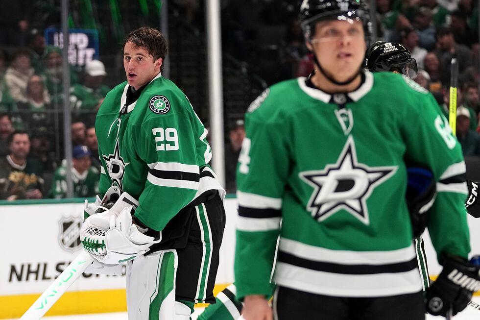 Dallas Stars goaltender Jake Oettinger, left, works to place his helmet back on after it was...