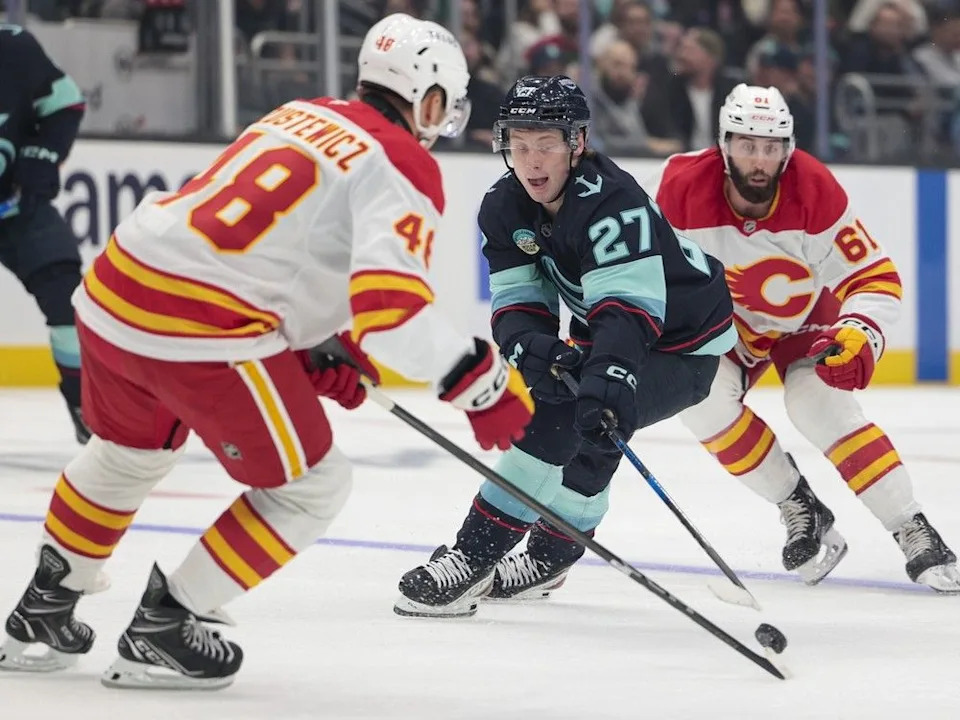  Seattle Kraken centre Berkly Catton (27) moves the puck as Calgary Flames defenceman Hunter Brzustewicz (48) and centre Clark Bishop (61) defend during the first period of a pre-season NHL hockey game, Sunday, Sept. 22, 2024, in Seattle.