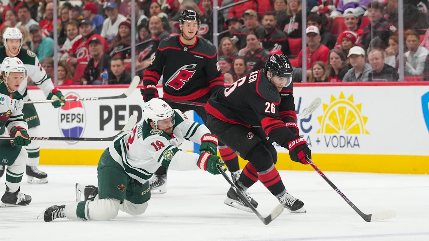 Nov 6, 2025; Raleigh, North Carolina, USA;  Minnesota Wild center Vinnie Hinostroza (18) and Carolina Hurricanes defenseman Sean Walker (26) battle over the puck during the second period at Lenovo Center. Mandatory Credit: James Guillory-Imagn Images