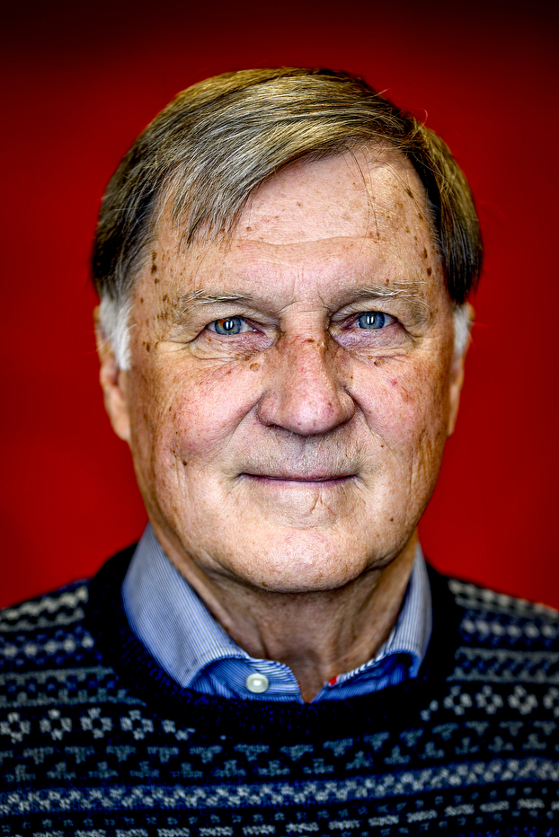 A portrait of a man with blue eyes and gray hair on a red background