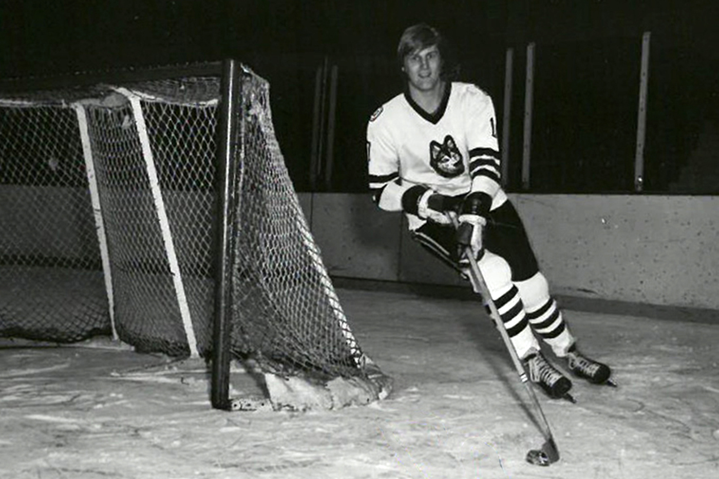A black and white photo of David Sherlock on the ice, skating around the goal