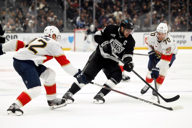 Kings captain Anze Kopitar, center, skates with the puck as...