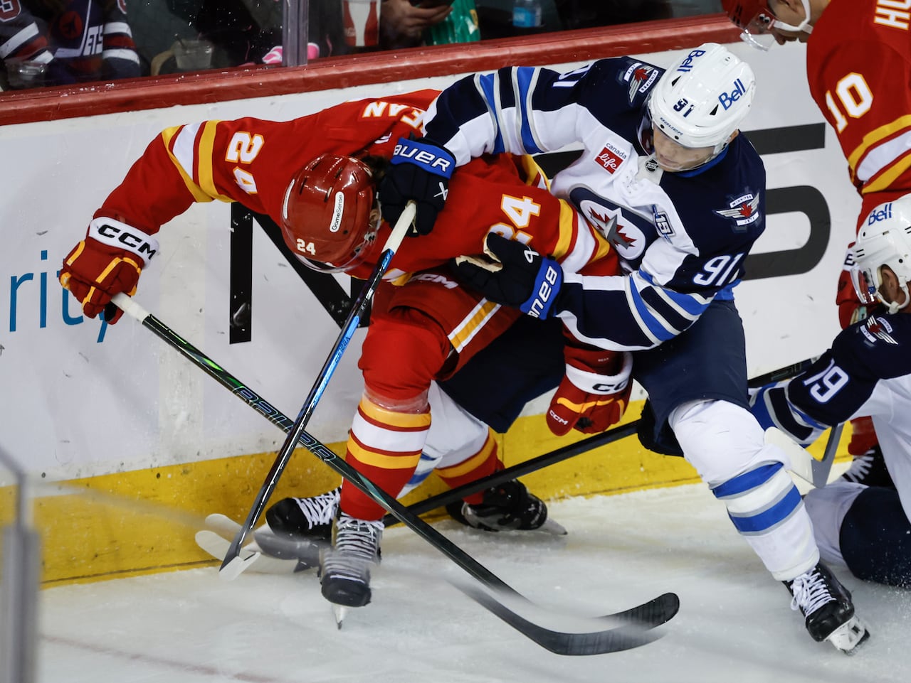 Hockey player in a white and blue jersey struggles with a player in a red and yellow jersey for the puck