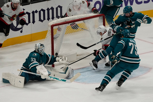 Ottawa Senators center Tim St&uuml;tzle (18) scores a goal past San Jose Sharks goaltender Alex Nedeljkovic (33), center Nick Cousins, top right, and right wing Ryan Reaves during the third period of an NHL hockey game in San Jose, Calif., Saturday, Nov. 22, 2025. (AP Photo/Jeff Chiu)