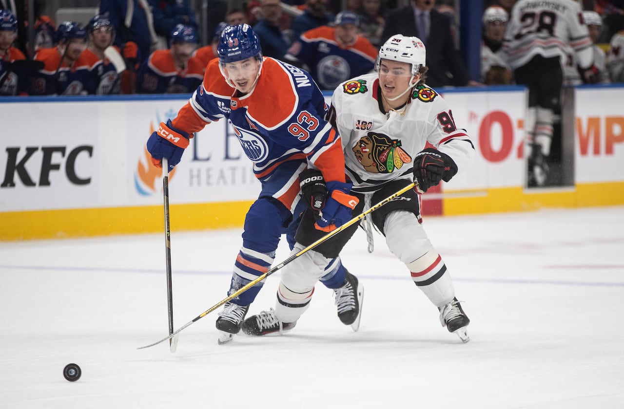 A hockey player wearing a blue jersey battles for the puck with a player wearing a white jersey.