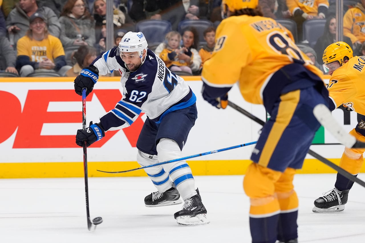 A hockey players fires the puck on net as he's chased down by a defender.