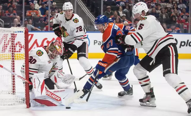 Chicago Blackhawks goalie Spencer Knight (30) makes a save on Edmonton Oilers' Connor McDavid (97) as Connor Murphy (5) defends and Alex Vlasic (72) looks for the rebound during second period NHL action, in Edmonton on Saturday, Nov. 1, 2025. (Jason Franson/The Canadian Press via AP)
