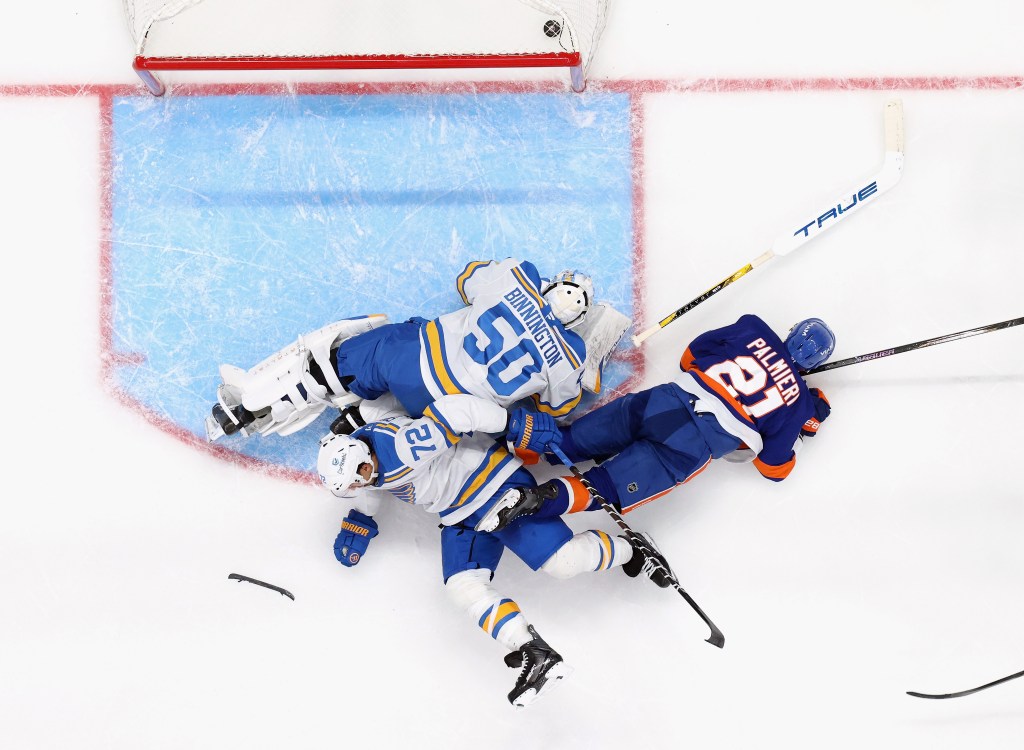 Overhead shot of two St. Louis Blues players, one a goalie, and one New York Islanders player fallen on the ice in front of the net. One of the Blues players has lost a skate blade.