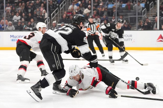 Kings defenseman Brandt Clarke, left, passes the puck over Ottawa...
