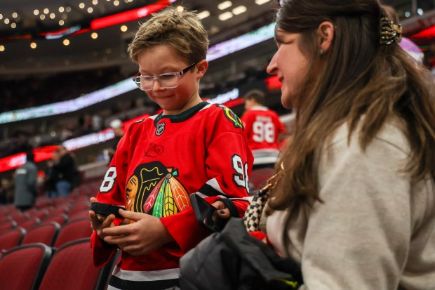 James Nelson, 8, inspects a puck that he received from a Calgary Flames player while his mother Jen Nelson of Mokena looked on before a game between the Blackhawks and Calgary Flames, Nov. 18, 2025, at the United Center. (Dominic Di Palermo/Chicago Tribune)