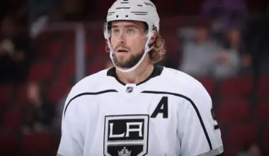 Adrian Kempe skating on the ice in a white Los Angeles Kings jersey during a game, showcasing his skill and leadership.