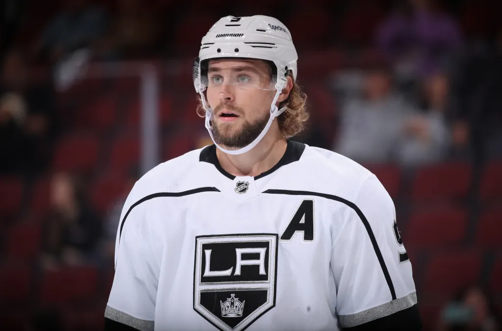 Adrian Kempe skating on the ice in a white Los Angeles Kings jersey during a game, showcasing his skill and leadership.