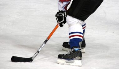 A hockey player on ice in black skates and blue-and-white socks controls a puck with a black stick, preparing to make a move during a game.