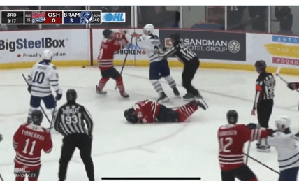 A hockey game in progress with Oshawa Generals and Brampton Beast players on the ice, one player from Oshawa is on the ground.