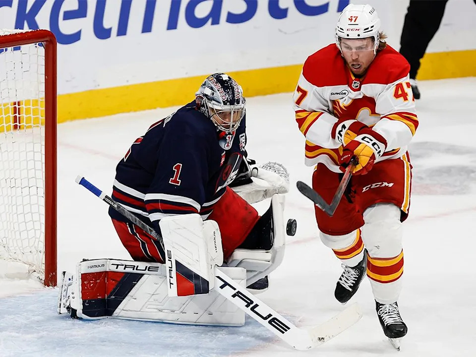  Calgary Flames forward Connor Zary (47) knocks down his own rebound off Winnipeg Jets goaltender Eric Comrie (1) during second-period NHL action in Winnipeg on Friday, Oct. 24, 2025.