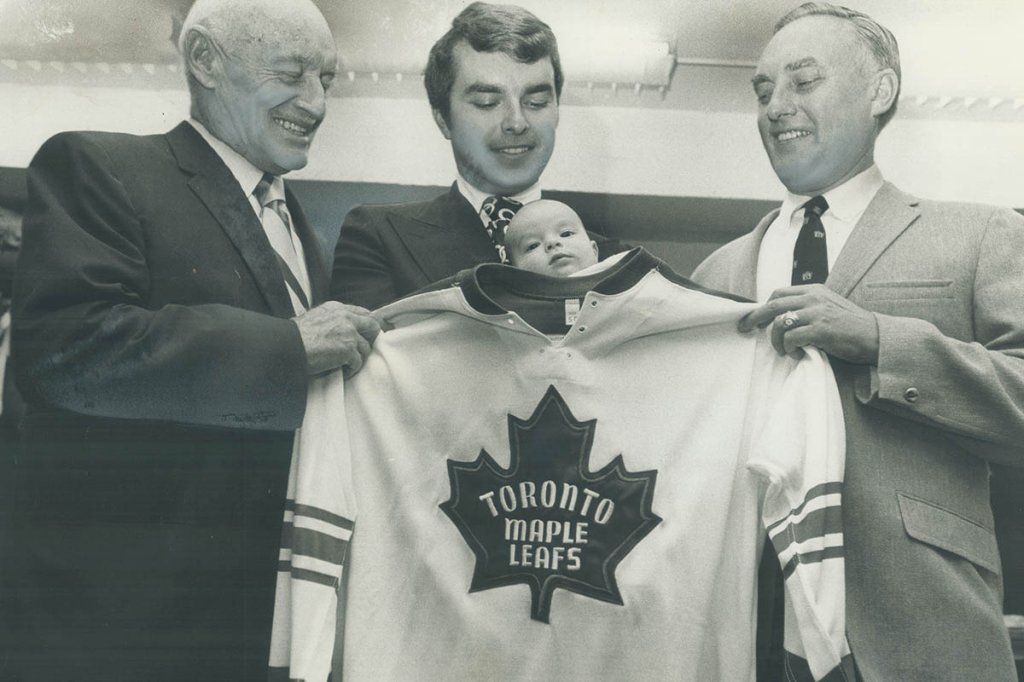 Another Smythe for the team. Thomas Brent Stafford Smythe; born July 11; gets a young look at his fu CANADA - JANUARY 01: Another Smythe for the team. Thomas Brent Stafford Smythe; born July 11; gets a young look at his future as proud father; grandfather and great-grandfather try oversized Toronto Maple Leaf hockey sweater on him. From left to right are great-grandfather Conn; founder of hockey dynasty; father Tommy Symthe; general manager of the Toronto Marlboros; and grandfather Stafford Smythe; president of the Maple Leaf hockey club. (Photo by Doug Griffin/Toronto Star via Getty Images)