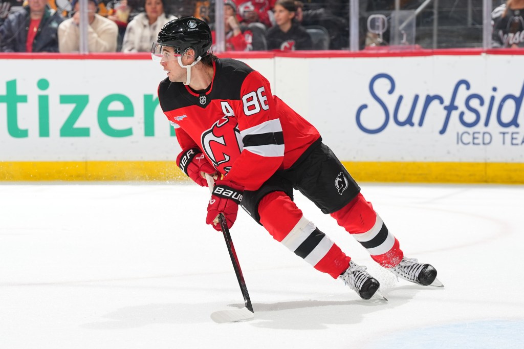 Jack Hughes of the New Jersey Devils skates with his hockey stick on the ice.