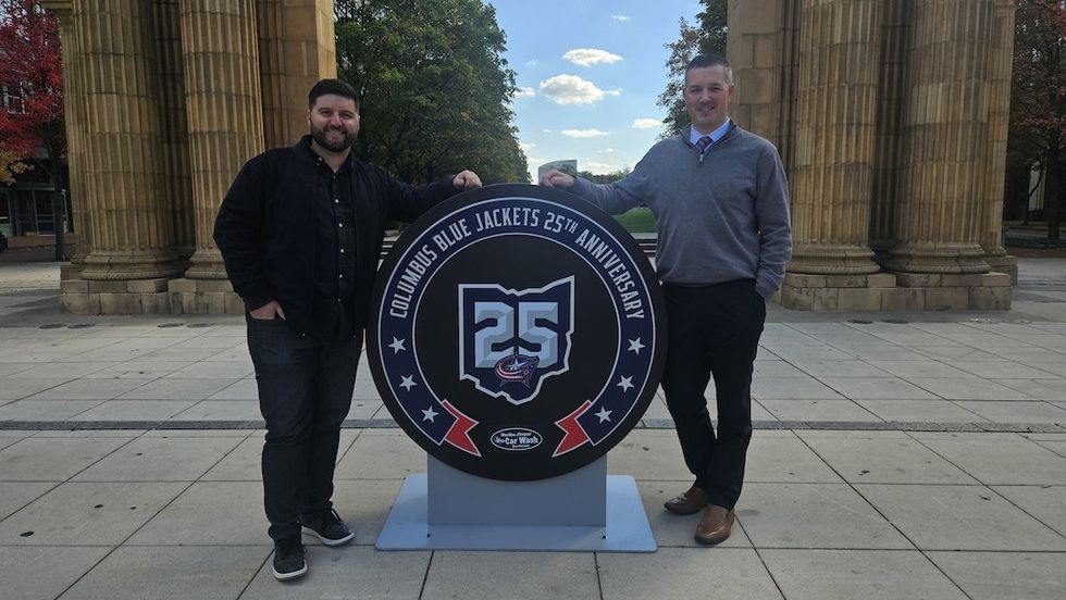Two men stand by a Columbus Blue Jackets 25th Anniversary display outdoors.