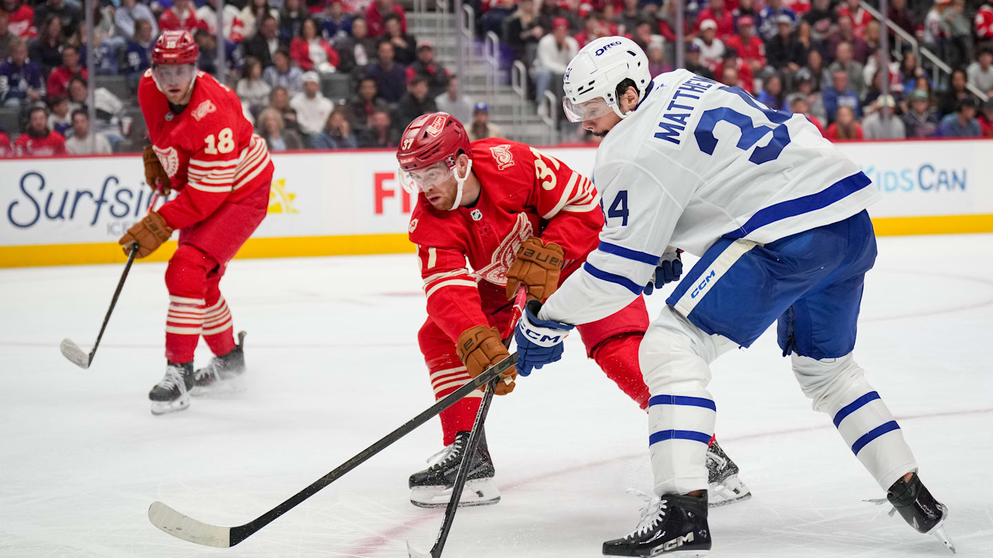 Detroit Red Wing forwards Andrew Copp (18) and J.T. Compher (37) battle Toronto Maple Leafs forward Auston Matthews (34) for the puck.