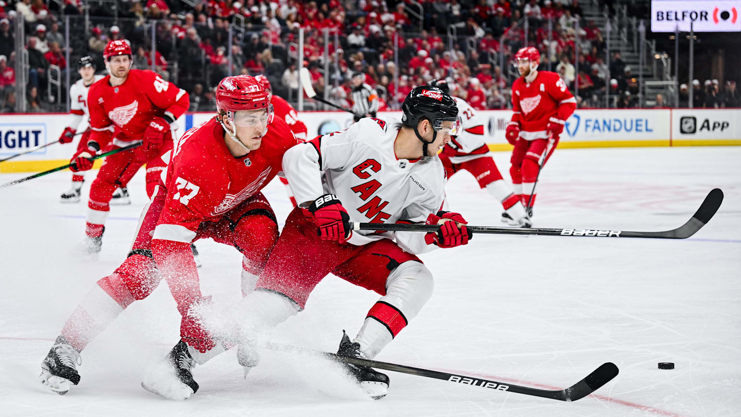 Apr 4, 2025; Detroit, Michigan, USA; Detroit Red Wings defenseman Simon Edvinsson (77) and Carolina Hurricanes center Jesperi Kotkaniemi (82) battle for the puck during the third period at Little Caesars Arena. Mandatory Credit: Tim Fuller-Imagn Images