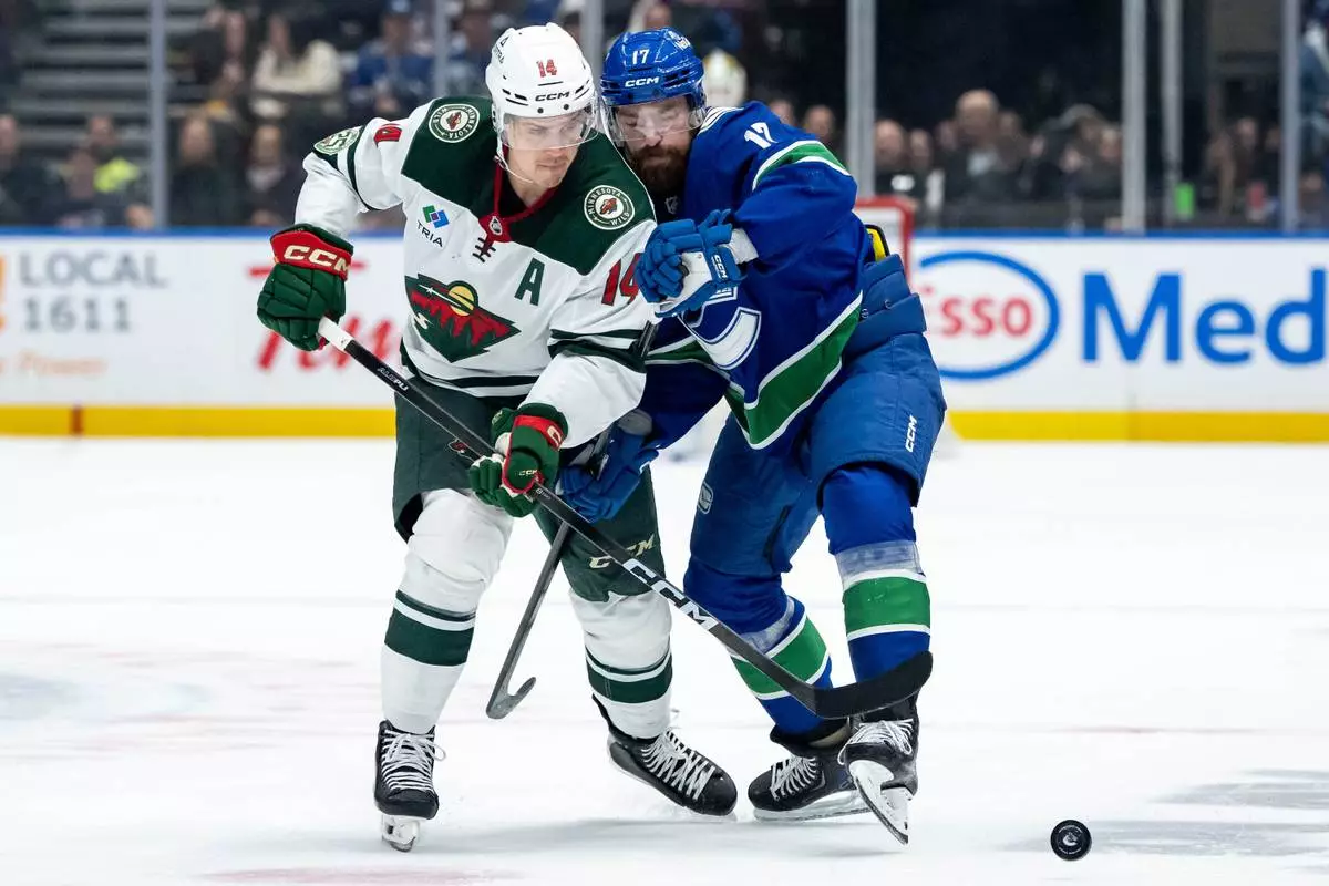 Minnesota Wild Joel Eriksson Ek (14) and Vancouver Canucks Filip Hronek (17) battle for the puck during second period NHL hockey action in Vancouver on Saturday, Dec. 6, 2025. (Ethan Cairns/The Canadian Press via AP)