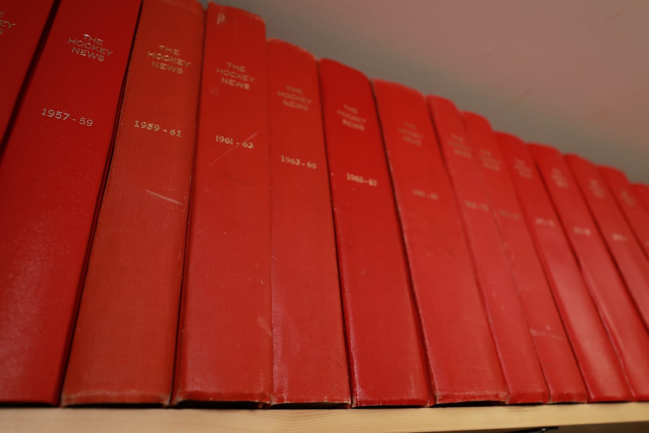 A close-up of red binders on a shelf with various years of The Hockey News listed on each spine.