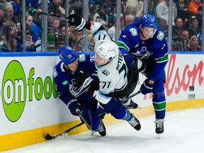 JJ Peterka #77 of the Utah Mammoth is checked by Elias Pettersson and Tyler Myers during the second period