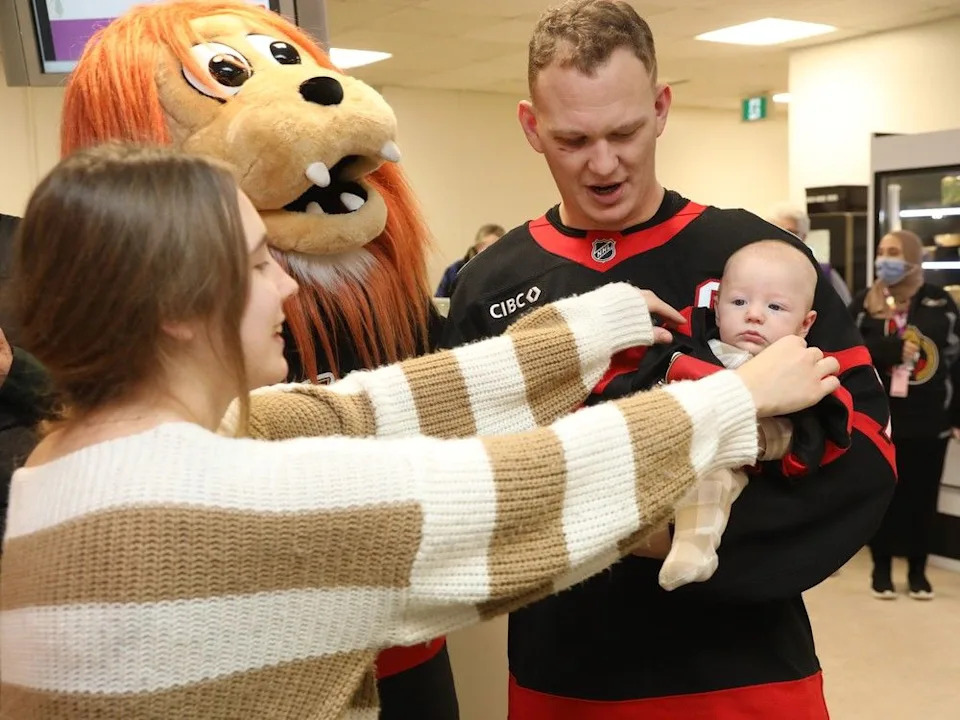 Brady Tkachuk and Spartacat of the Ottawa Senators are photographed 2.5 months old Ollie Matteo Mallabone-Bérubé as mom Anna Mallabone fixes Ollie’s sense jersey for the photo.