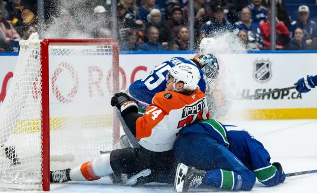 Philadelphia Flyers' Owen Tippett (74) and Vancouver Canucks' Elias Pettersson, right, slide into goaltender Thatcher Demko (35) during the second period of an NHL hockey game in Vancouver, B.C., Tuesday, Dec. 30, 2025. (Ethan Cairns/The Canadian Press via AP)