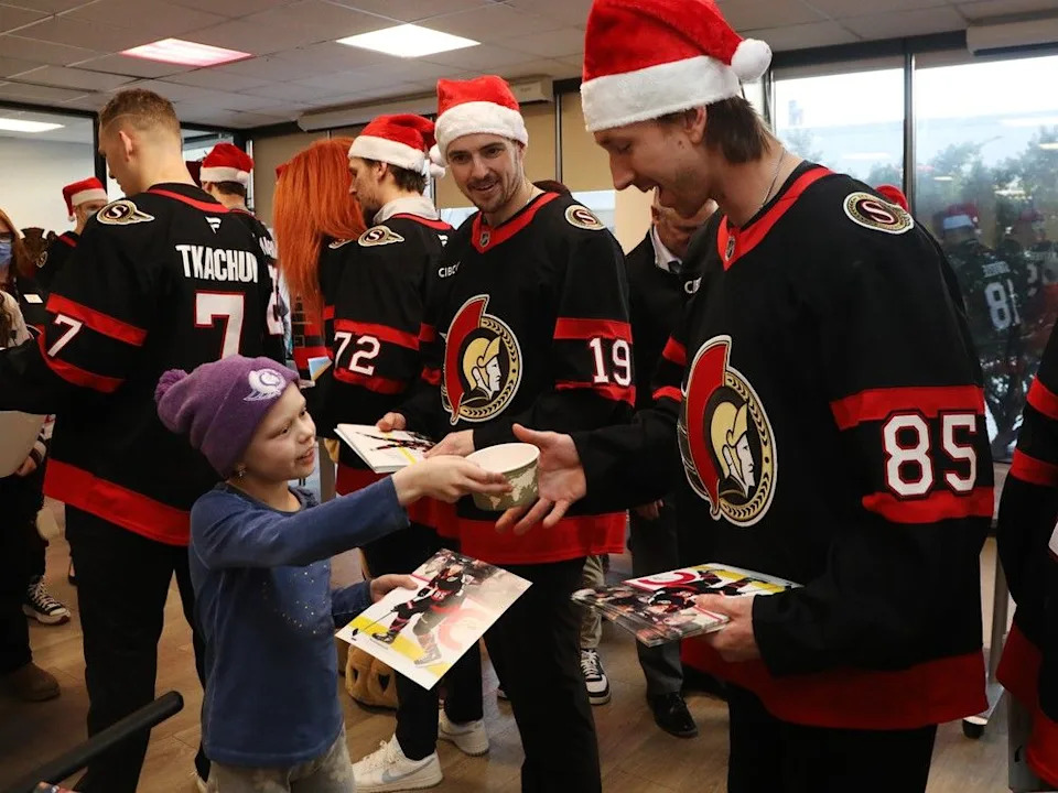  Charlotte Dow, 9 years old, gives a snack to Jake Sanderson of the Ottawa Senators during their annual their annual trip to the Children’s Hospital of Eastern Ontario (CHEO) to spread festive cheer, December 08, 2025.