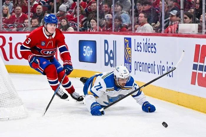  Mathieu Joseph of the St. Louis Blues falls to the ice skating to the puck against Cole Caufield of the Montreal Canadiens during the third period at the Bell Centre on Sunday, December 7, 2025.