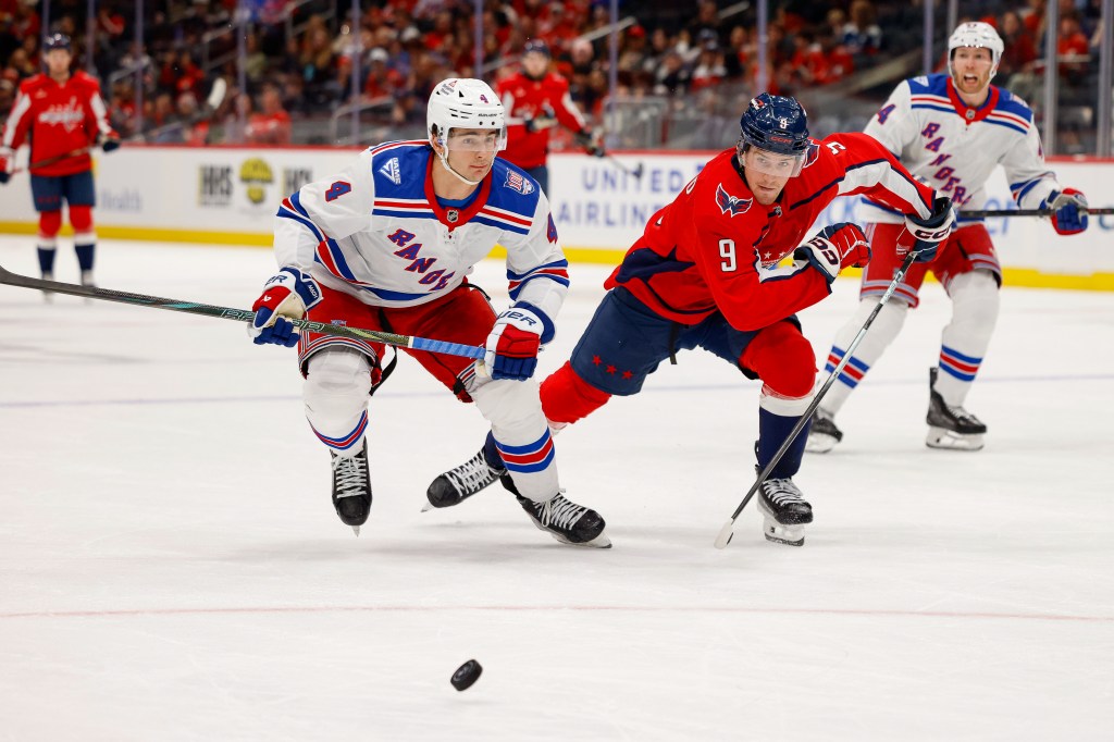 Ryan Leonard of the Washington Capitals and Braden Schneider of the New York Rangers race for a loose puck.