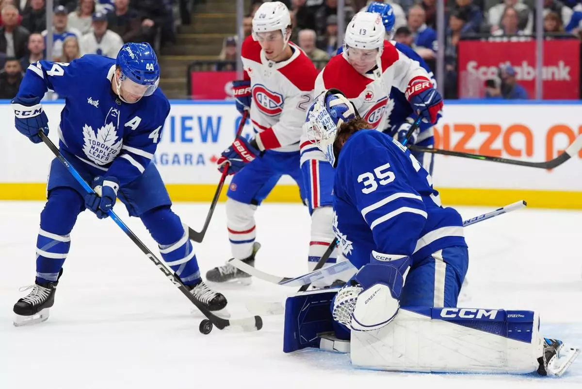 Toronto Maple Leafs defenceman Morgan Rielly (44) clears the puck from in front of his goalie Dennis Hildeby (35) as Montréal Canadiens left wing Juraj Slafkovský (20) and Canadiens right wing Cole Caufield (13) look on during first period NHL hockey action in Toronto on Saturday, Dec. 6, 2025. (Frank Gunn/The Canadian Press via AP)