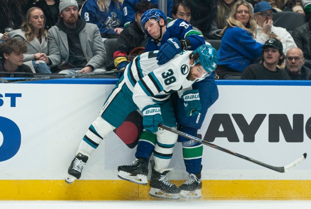 VANCOUVER, CANADA - DECEMBER 27: Mario Ferraro #38 of the San Jose Sharks takes out Marco Rossi #93 of the Vancouver Canucks along the side board during the first period of NHL action at Rogers Arena on December 27, 2025 in Vancouver, Canada. (Photo by Rich Lam/Getty Images)