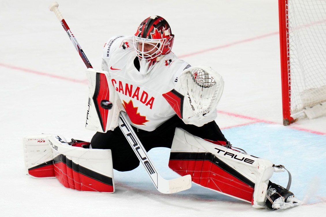 Goalie in white jersey with red maple leaf goes into splits to make a save