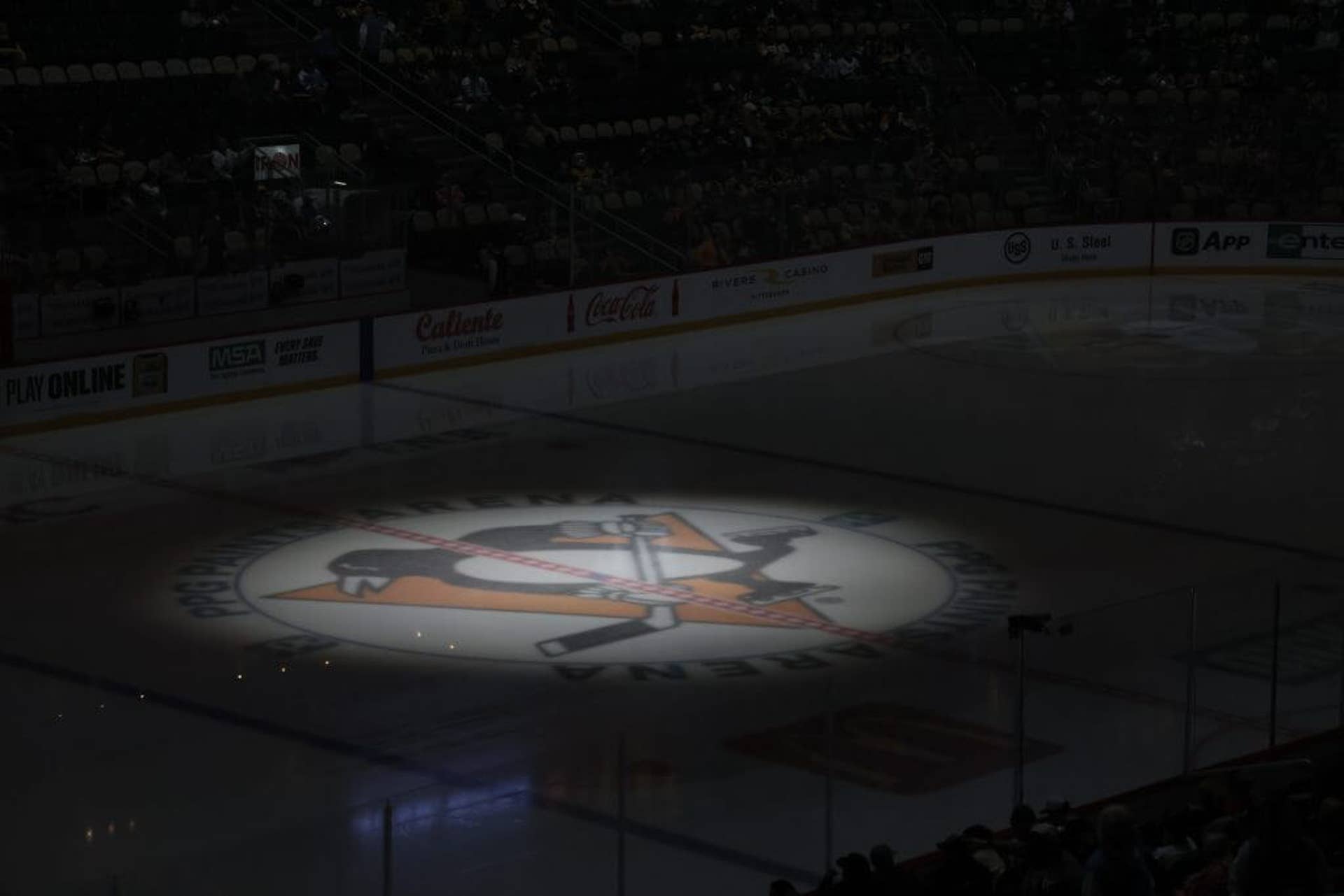 Penguins logo illuminated by spotlight at center ice