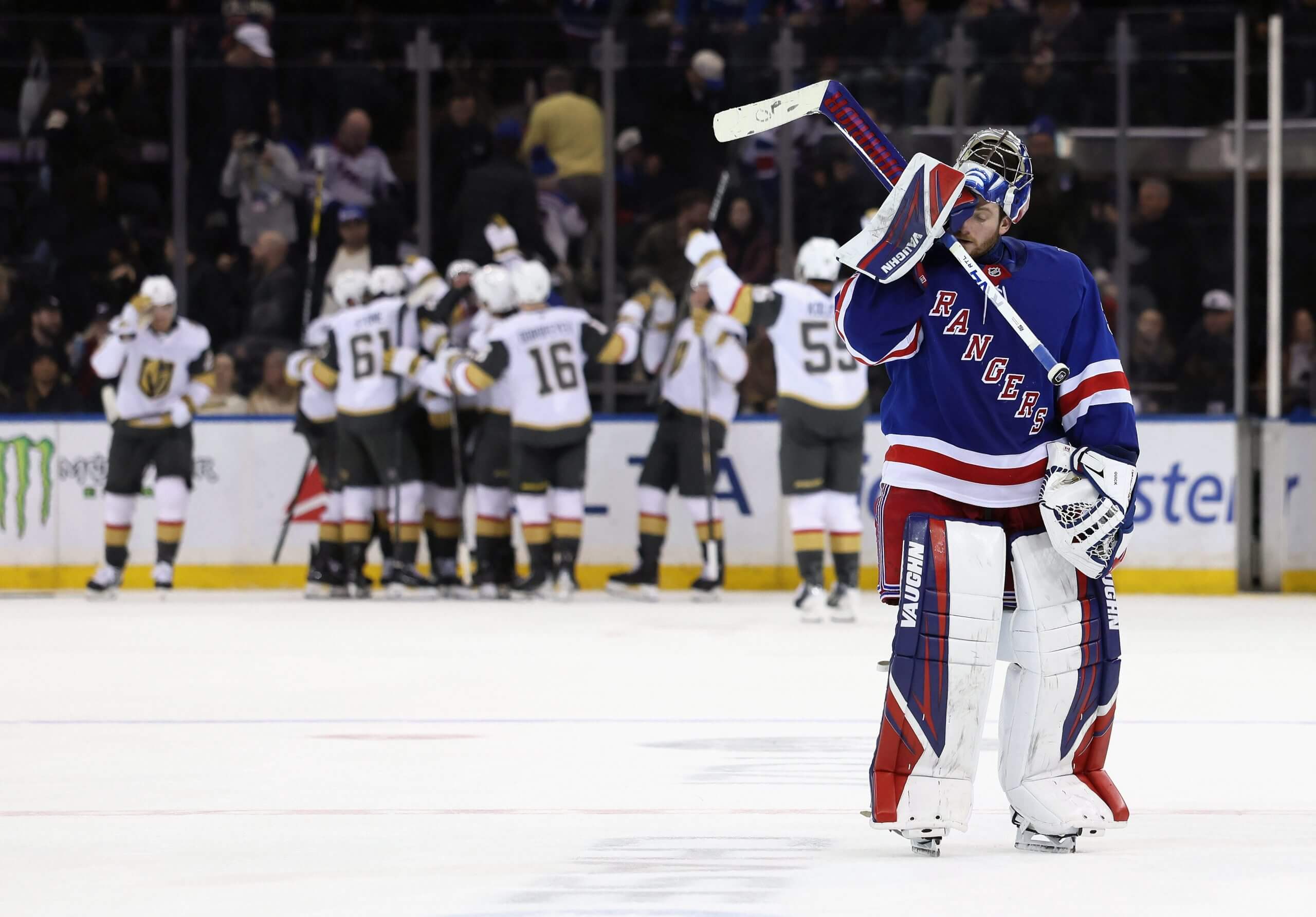 Rangers goalie Jonathan Quick rubs his face leaving the ice with Vegas players celebrating in the distance.