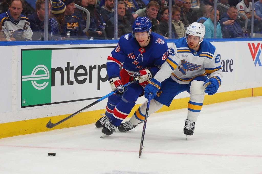 Two hockey players, one from the New York Rangers and one from the St. Louis Blues, skating on the ice with a puck nearby.