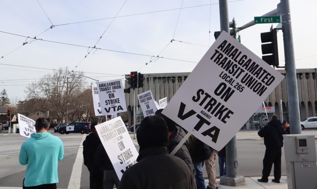 Group of people standing at First Street intersection, all holding white signs with black text reading "Amalgamated Transit Union Local 265 On Strike against VTA"