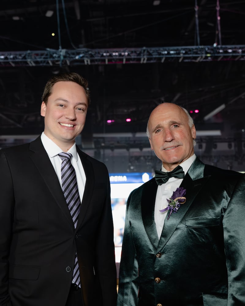 Josh Schaefer and Daryl Evans pose for a photo from Crypto.com Arena. Schaefer wears a black suit with a striped blue tie, while Evans wears a velvet green suit with matching bowtie.