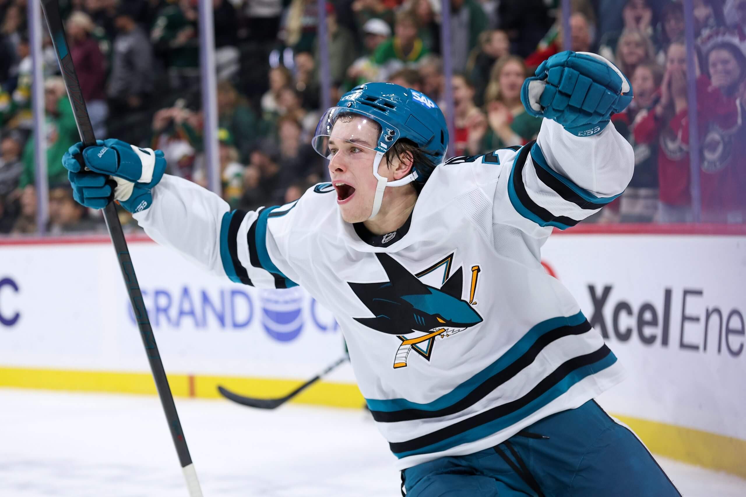The Sharks' Macklin Celebrini raises both arms in celebration.