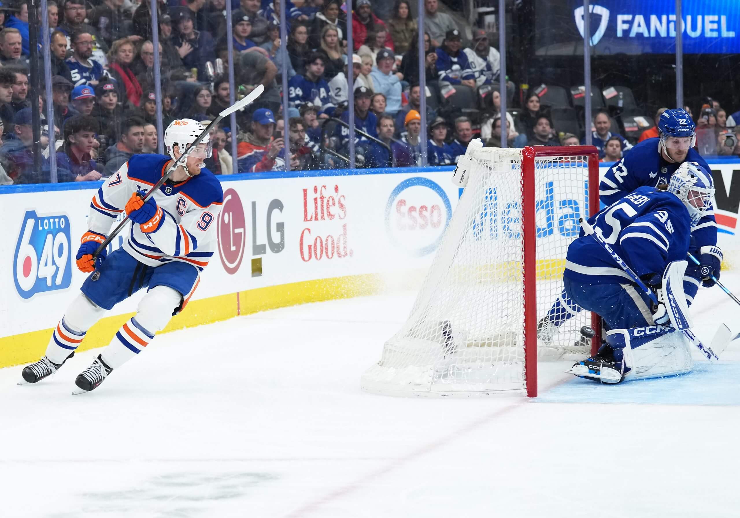 Edmonton Oilers center Connor McDavid, left, skates behind the Toronto Maple Leafs net with a goalie and another Maple Leaf in front.