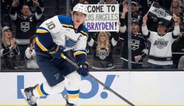 St. Louis Blues captain Brayden Schenn (#10) skates with the puck past tall rink boards featuring a Coca-Cola advertisement. Behind the glass, Los Angeles Kings fans cheer, and a woman holds up a handmade sign that reads "COME TO LOS ANGELES BRAYDEN!".