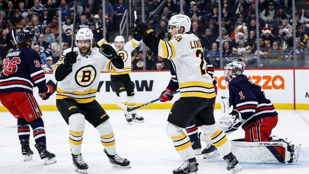 Boston Bruins' Elias Lindholm (28) and Pavel Zacha (18) celebrate David Pastrnak's goal against Winnipeg Jets goaltender Eric Comrie (1) during the first period of an NHL hockey game in Winnipeg, Manitoba, Thursday, Dec. 11, 2025. (John Woods/The Canadian Press via AP)
