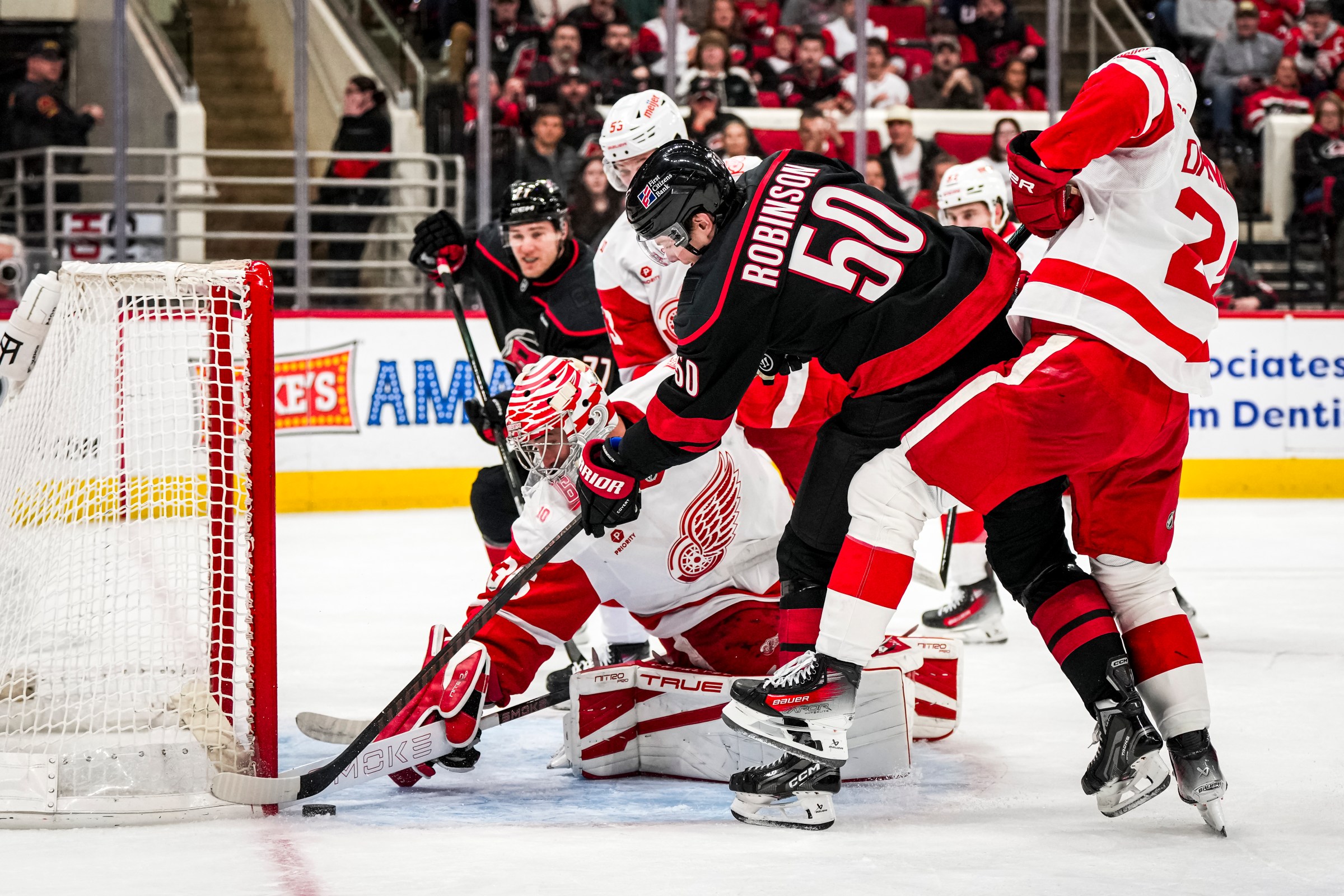 RALEIGH, NORTH CAROLINA - DECEMBER 27: Goaltender John Gibson #36 of the Detroit Red Wings defends the net as Eric Robinson #50 of the Carolina Hurricanes reaches for a loose puck in the first period of a game at Lenovo Center on December 27, 2025 in Raleigh, North Carolina. (Photo by Josh Lavallee/NHLI via Getty Images)