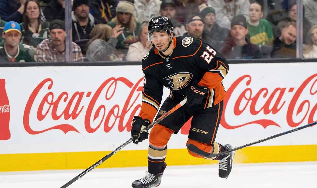 A hockey player, Jordan Kyrou, wearing the black Anaheim Ducks uniform with number 25, is skating with the puck on the ice during a game.