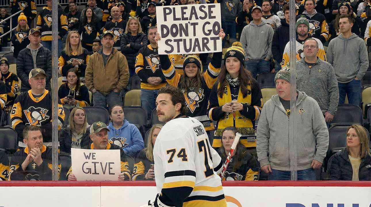 Stuart Skinner, wearing his white #74 Pittsburgh Penguins jersey, stands on the ice looking towards the fans behind the plexiglass. A fan in the center holds up a white sign with black letters that reads "PLEASE DON'T GO STUART".