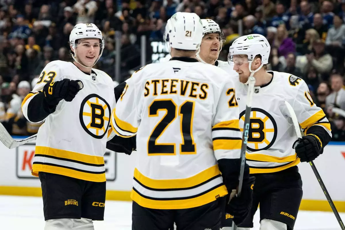 Boston Bruins' Fraser Minten, left, celebrates after his goal against the Vancouver Canucks with Alex Steeves (21), Hampus Lindholm (27), and Casey Mittelstadt (11) during the first period of an NHL hockey game in Vancouver, British Columbia, Saturday, Jan. 3, 2026. (Ethan Cairns/The Canadian Press via AP)