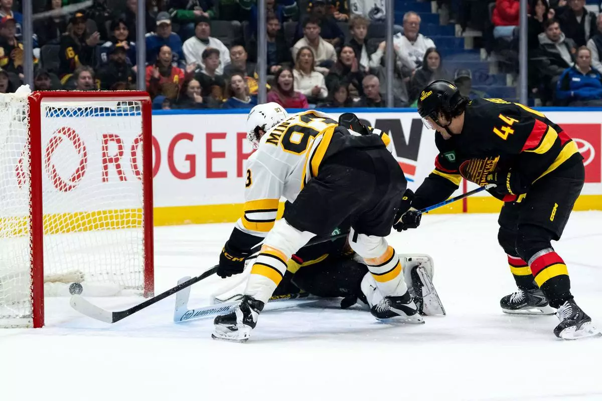 Boston Bruins' Fraser Minten (93) scores on Vancouver Canucks goaltender Kevin Lankinen (32) as Kiefer Sherwood (44) defends during overtime in an NHL hockey game in Vancouver, British Columbia, on Saturday, Jan. 3, 2026. (Ethan Cairns/The Canadian Press via AP)